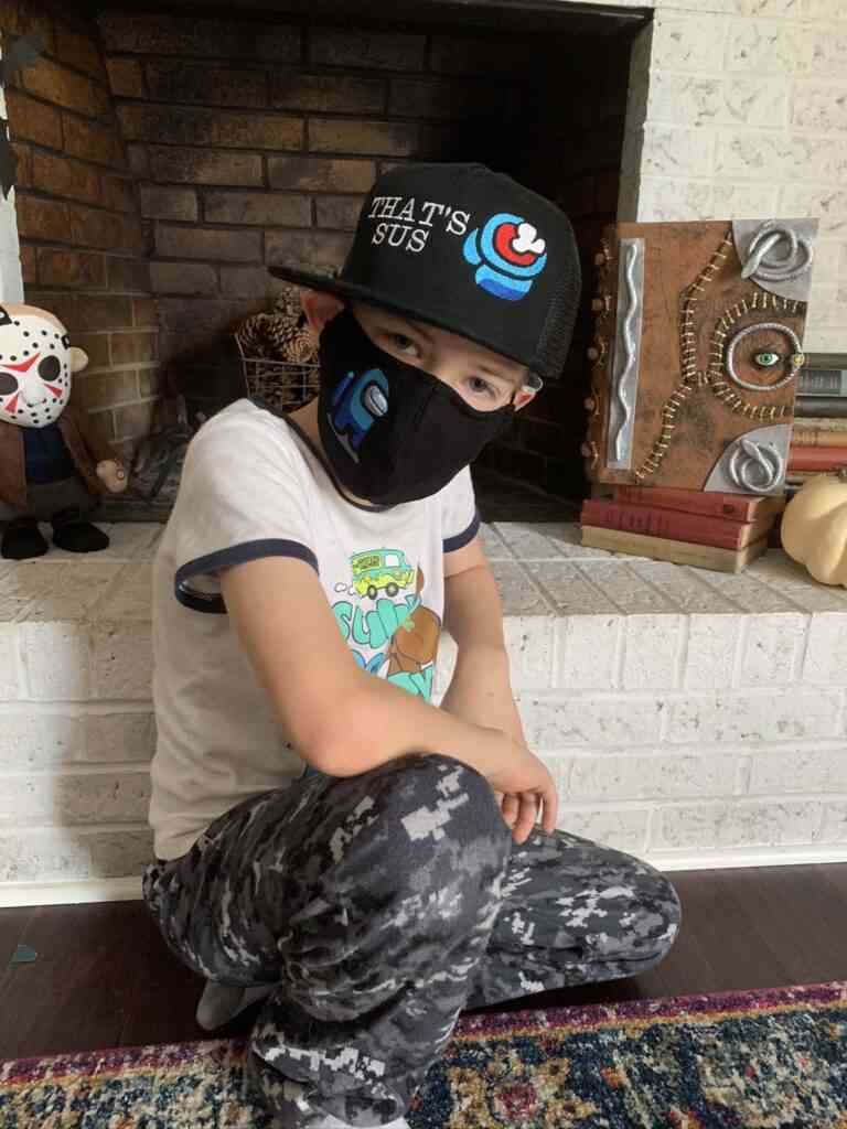 Among Us Face Mask: A young boy sitting on the floor wearing an Among Us Face Mask.