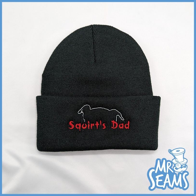 A black beanie with the word squirt's dad on it.