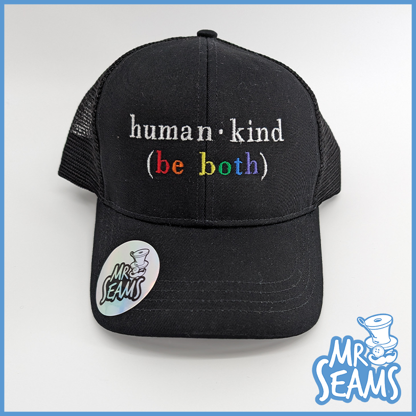 Black beanies with the phrase "Human - Kind (Be Both)" embroidered in colorful letters and a "Mr. Seams" sticker on the brim.